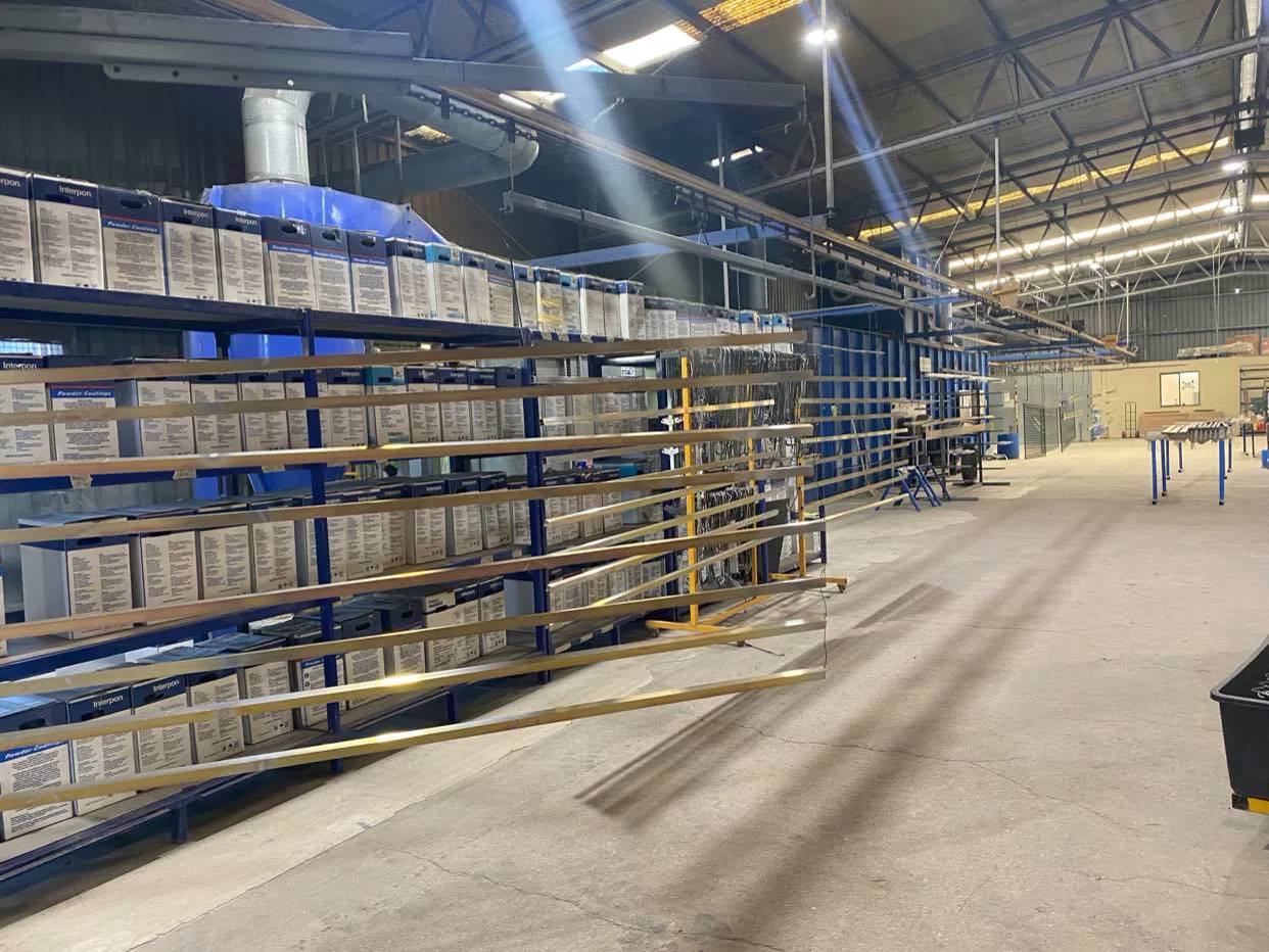 Racked powder stock and the coating line at the OZ Coat workshop with overhead conveyor rails and racked powder stock
